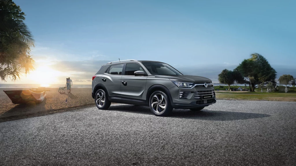 KGM E-Korando parkert ved en strand med solnedgang og mennesker i bakgrunnen.